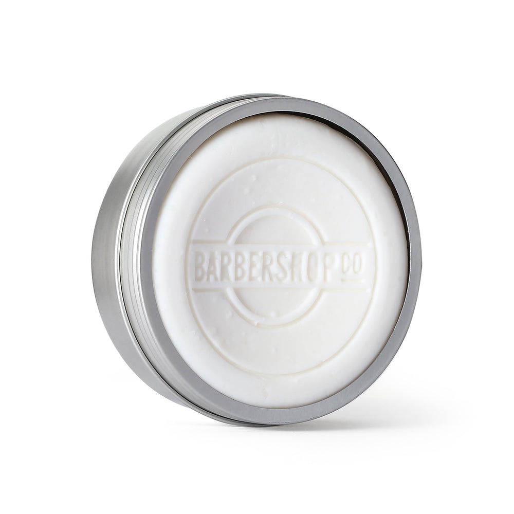 White shave soap embossed with the BarberShopCo logo in an open silver tin.